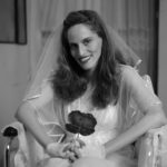 Woman in wedding dress smiling to camera holding bouquet in wheelchair